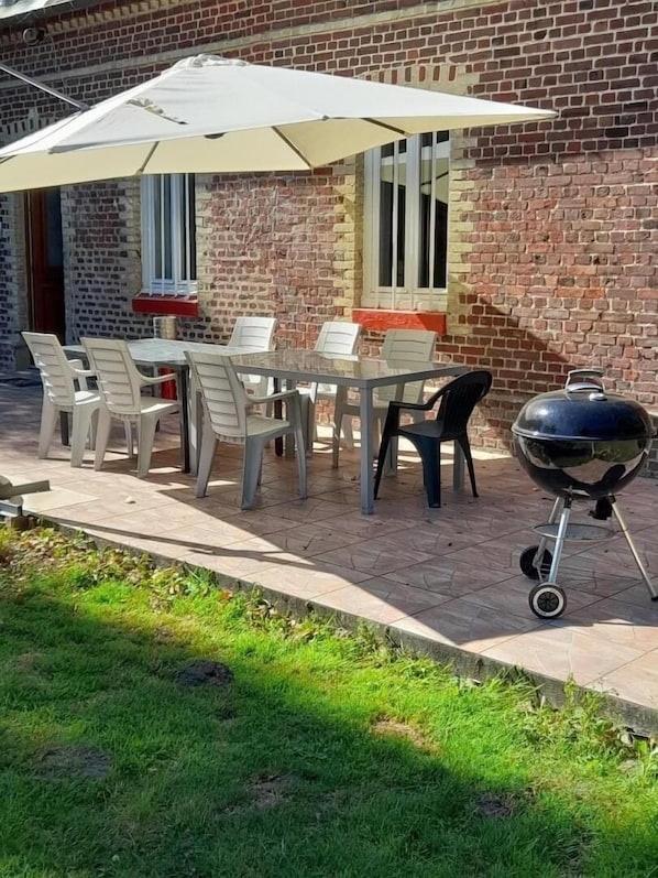 A patio with a table and chairs, a barbecue grill, and a brick wall.