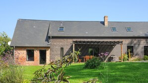 Une maison à deux étages avec un patio couvert, une partie en briques sur le côté gauche et une cour gazonnée.