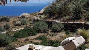 A seaside lounge area with two sunbeds, a woven parasol, and a view of the sea. - Ivy's Natural Resort (Tinos)