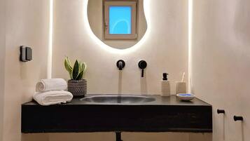 Casa de banho com lavatório preto, espelho com tela azul, planta em vaso e artigos de higiene pessoal.