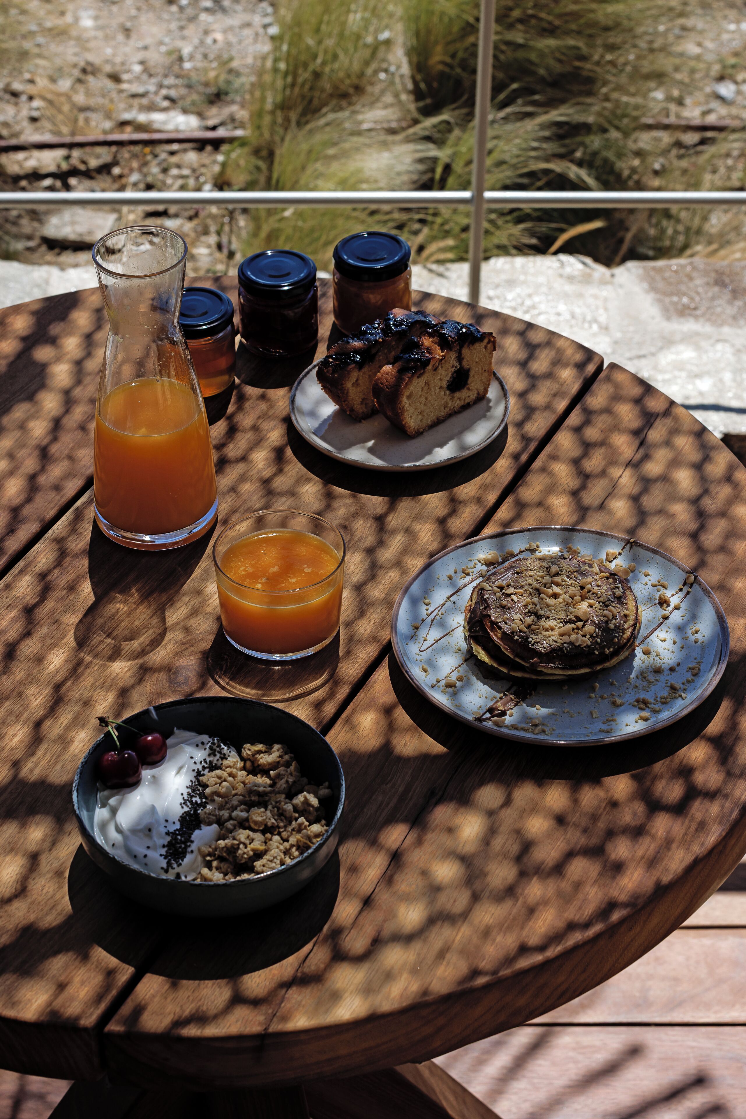 A wooden table with a variety of food items including a glass of orange juice, a bowl of cereal with fruit, and a plate with a dessert.