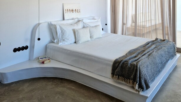Une chambre à coucher moderne avec un lit aux lignes courbes, une table de chevet, une lampe suspendue et des rideaux transparents.