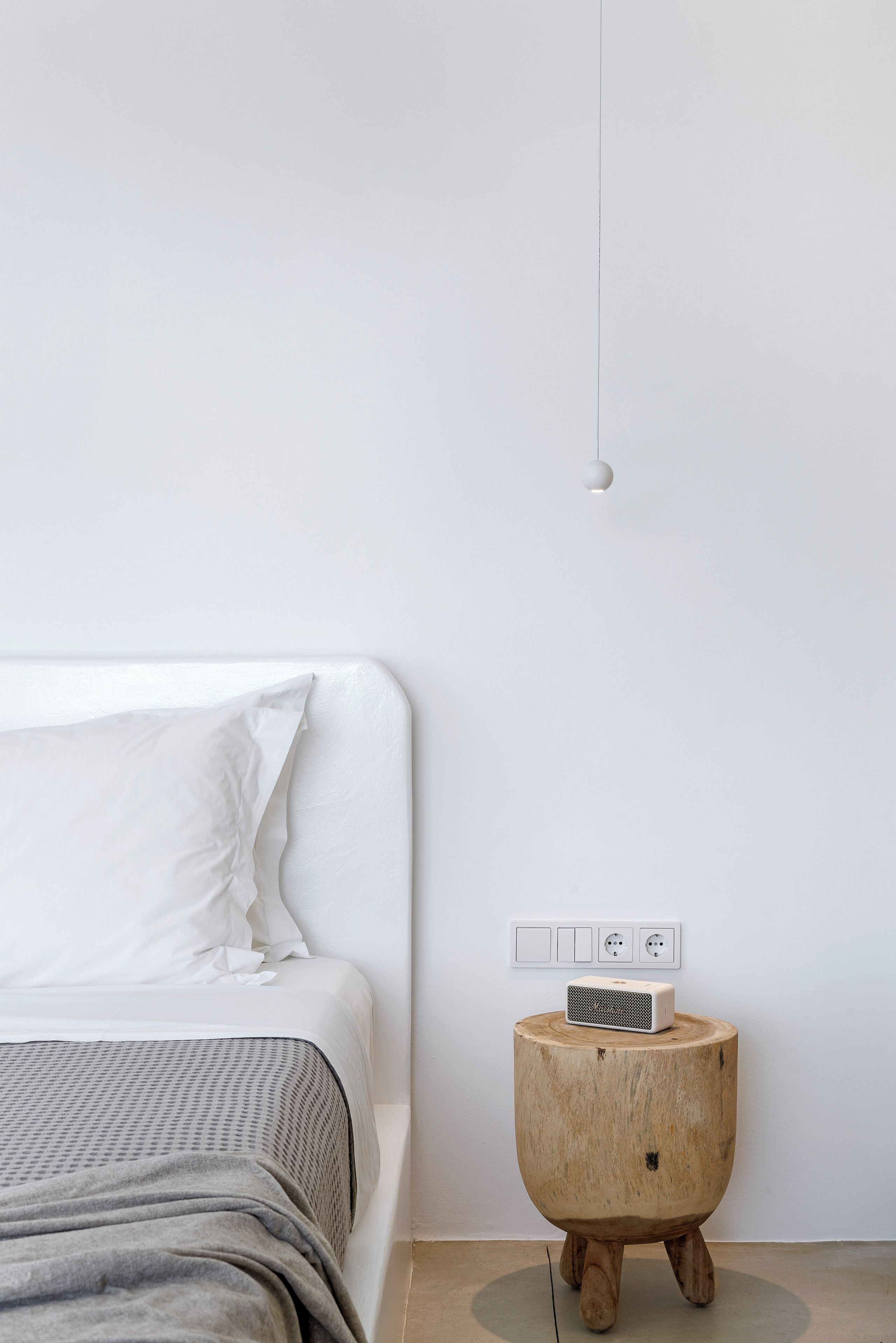 A minimalist bedroom with a bed, a bedside table with a power strip, and a hanging light fixture.