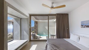 A bedroom with a large bed, a ceiling fan, a sliding glass door leading to a pool area, and a stone wall in the background. - Ivy's Natural Resort (Tinos)