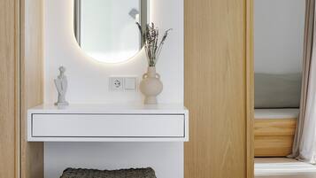 Un dormitorio moderno con un tocador de madera, un espejo redondo y una mesita de noche con un florero.