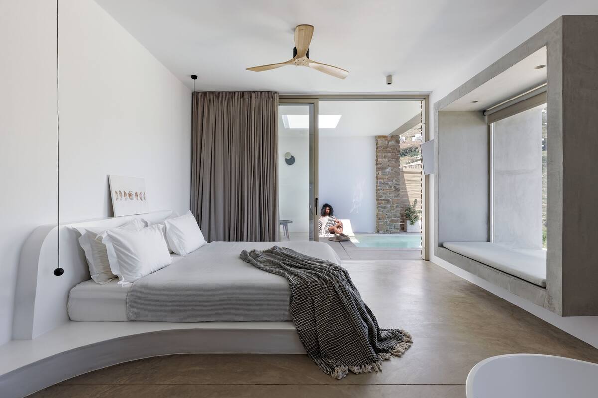 Un dormitorio moderno con una cama curvada, ventilador de techo y vistas a una piscina y zona exterior.