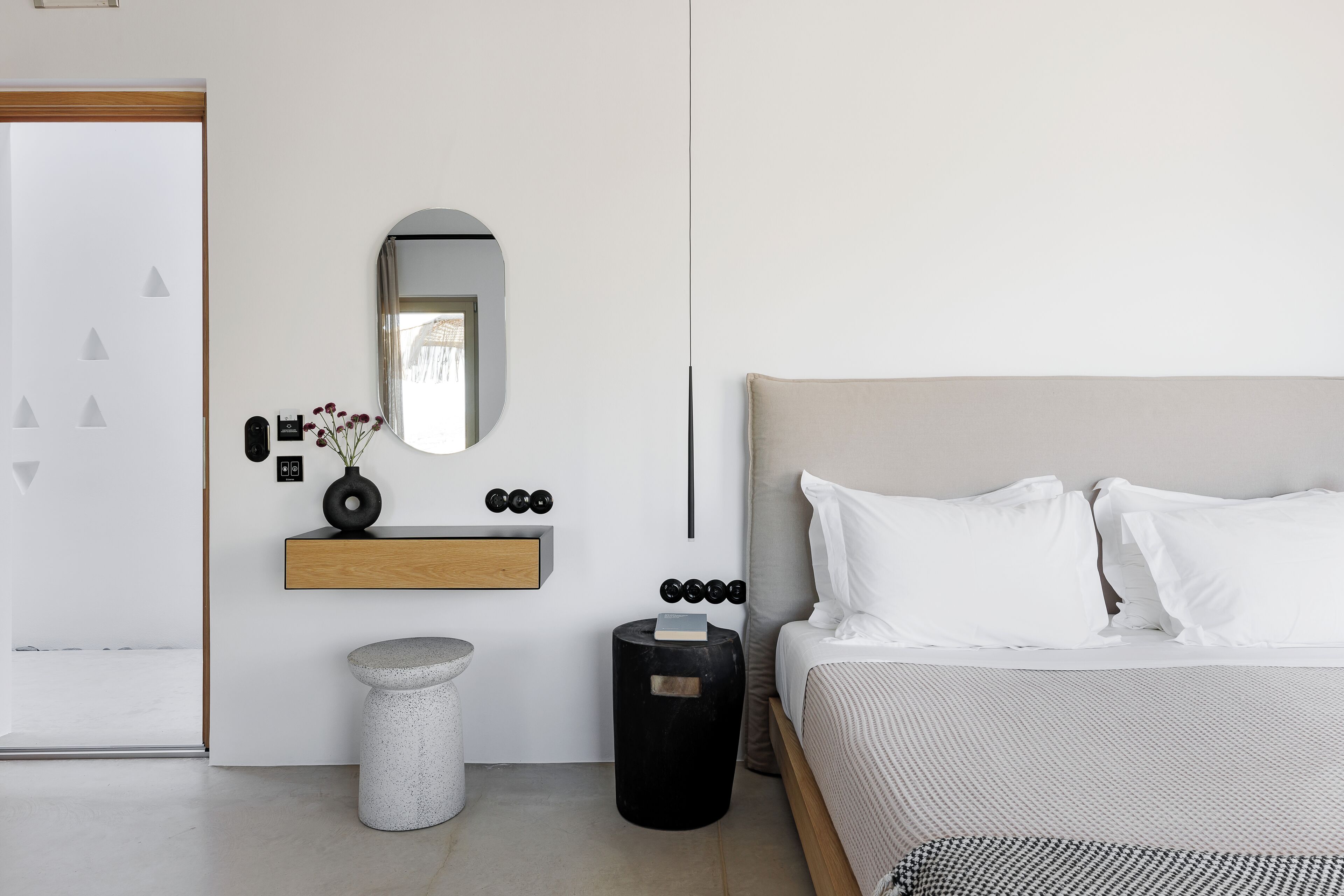 A modern bedroom with a bed, a bedside table, a mirror, and a small shelf with decorative items.
