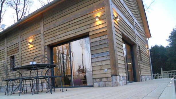 A wooden cabin with a deck, a table, and chairs.