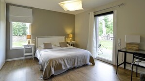 A bedroom with a large bed, bedside tables with lamps, a desk with a chair, and a sliding glass door to the outside.