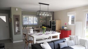 A modern living room with a black sofa, a dining table set for four, and a kitchen in the background.