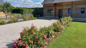 A wooden building with a gravel driveway and a garden with pink roses.