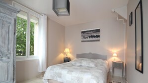 A bedroom with a bed, two bedside lamps, a window, a picture on the wall, and a wardrobe.