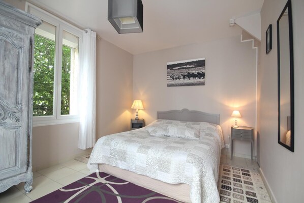 A bedroom with a bed, two bedside lamps, a window, a picture on the wall, and a wardrobe.