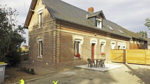A two-story brick house with a sloped roof, a front porch with a table and chairs, and a wooden fence in the background.