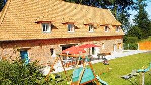 Ein zweistöckiges Ziegelhaus mit geneigtem Dach, einer Schaukel und einer Terrasse mit Gartenmöbeln.