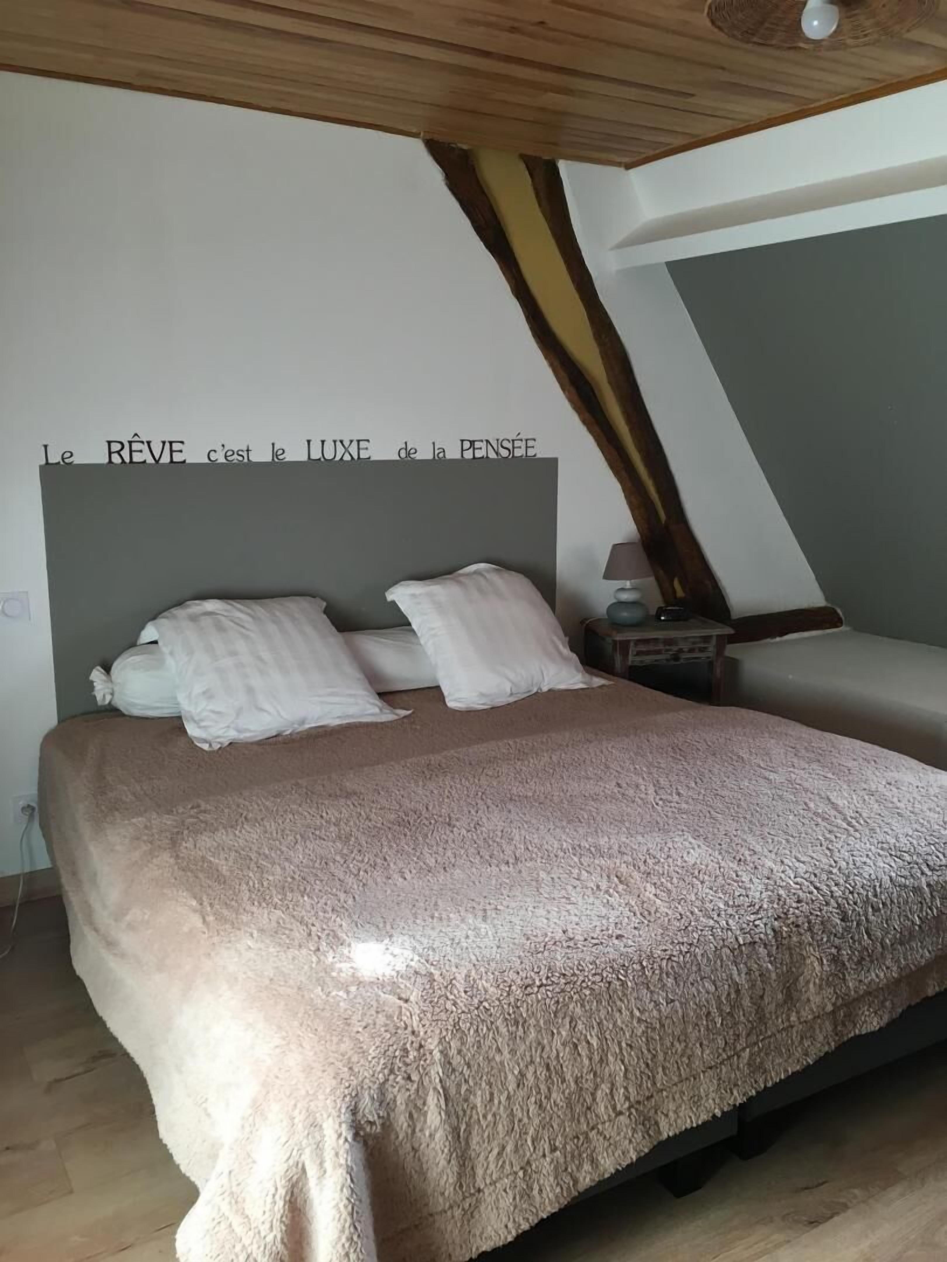 A bedroom with a large bed, a headboard with a quote, and a sloped ceiling.