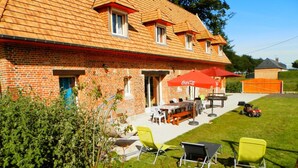 Ein Backsteinhaus mit einer Terrasse, die Gartenmöbel und einen roten Sonnenschirm zeigt.
