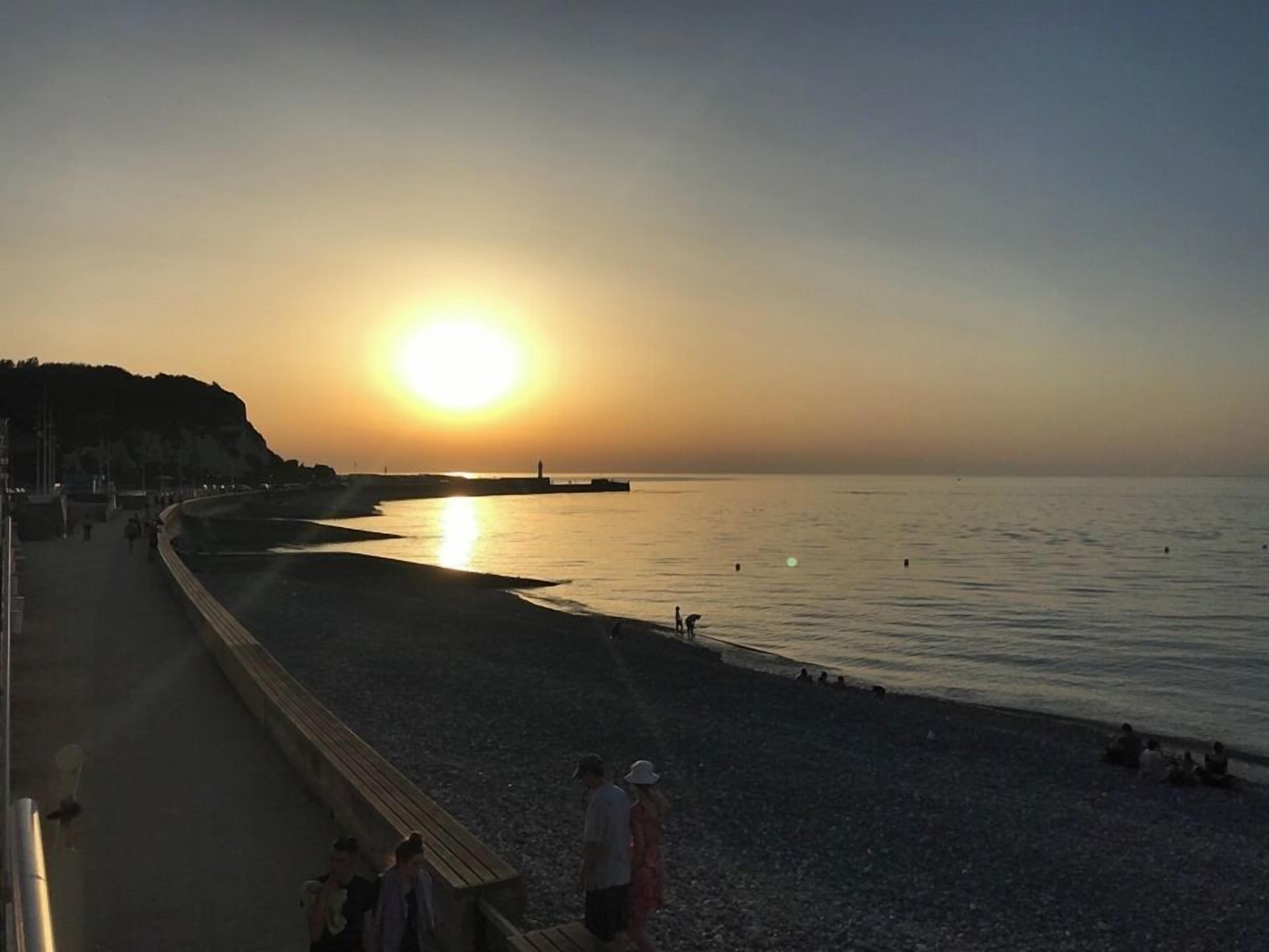 A beach scene with a sunset, calm sea, and a promenade.