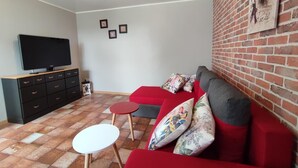 Una sala de estar con un sofá rojo, un televisor sobre un mueble de madera y una mesita blanca.