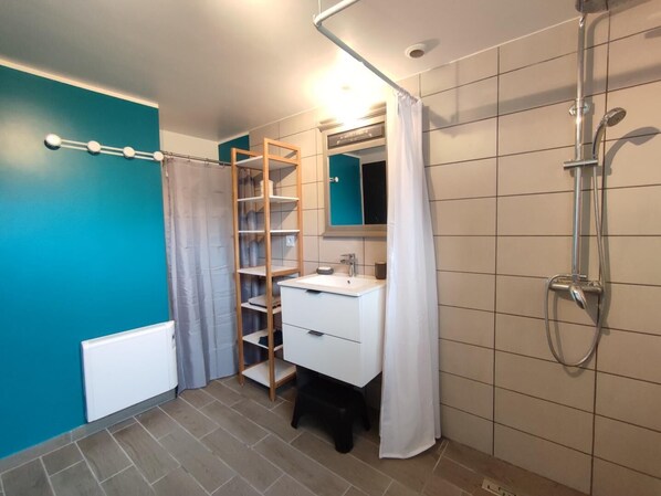 A bathroom with a white sink, a shower, a towel rack, and a wooden shelf unit.