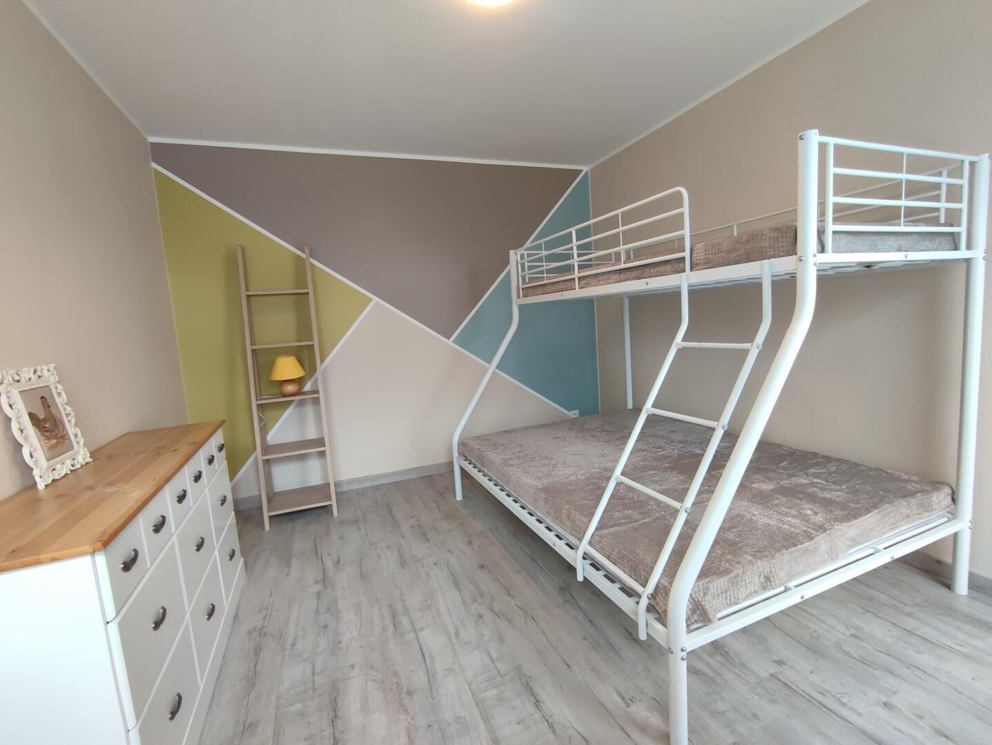 A bunk bed room with a wooden dresser and a ladder.