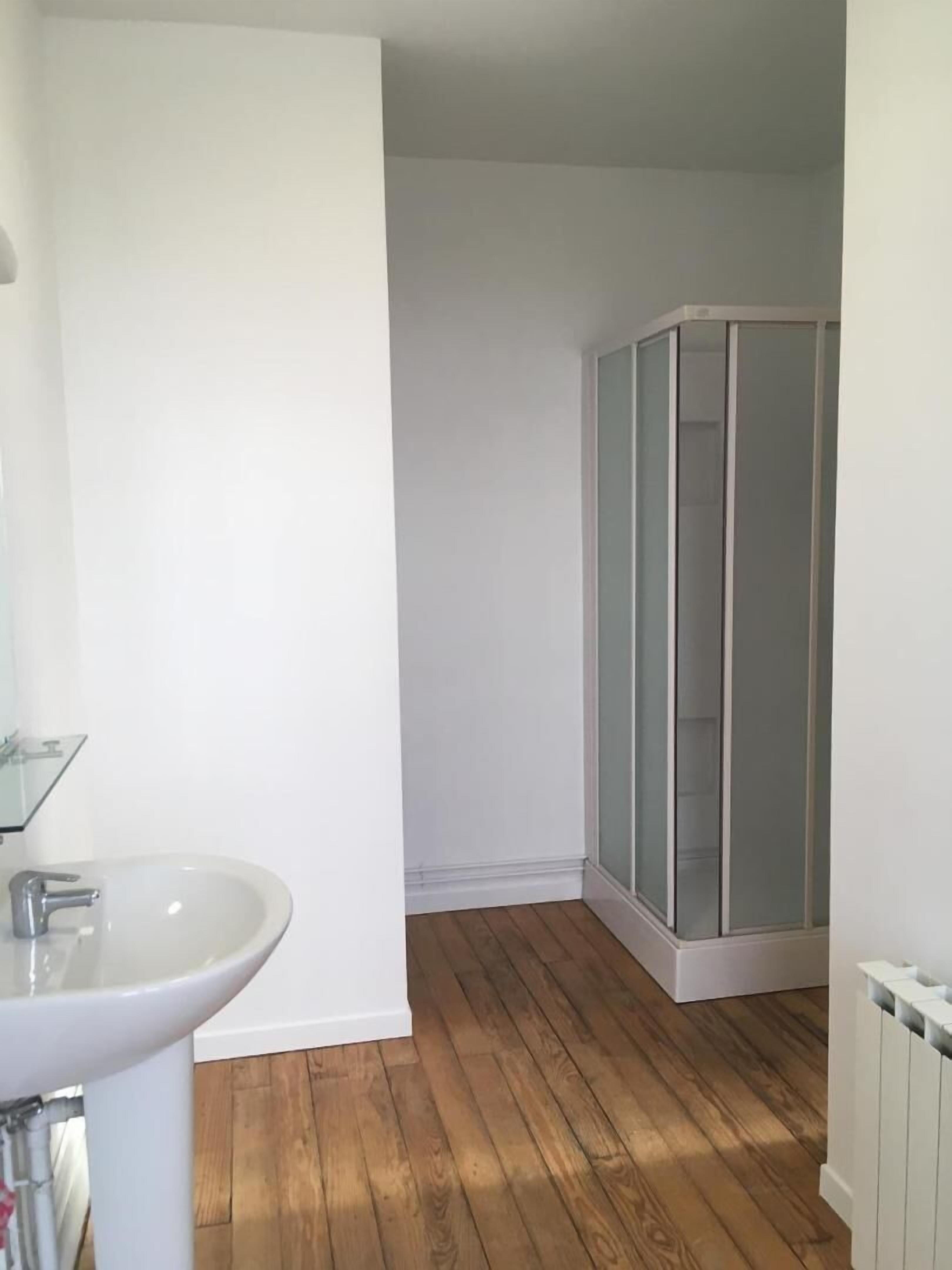 A bathroom with a white sink, wooden flooring, and a glass shower enclosure.