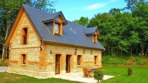 Ein Steinhaus mit schrägem Dach, mehreren Fenstern und einem kleinen Garten.