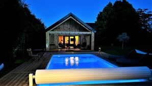 Eine Holzhütte mit Pool, Sitzgelegenheiten im Freien und einem gut beleuchteten Innenraum.