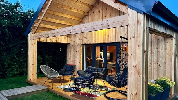 Eine Holzhütte mit einer Veranda, zwei schwarzen gepolsterten Stühlen, einem weißen Stuhl und einem Hängesessel.