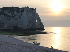 A beach with white cliffs, a boat on the shore, and a person standing by the water.