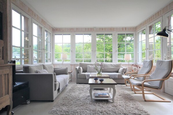 A spacious living room with a large window, a sofa, a coffee table, and two armchairs.