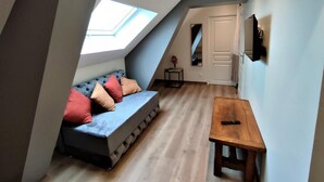 Une chambre de style « loft » avec un plafond en pente, un canapé intégré avec des coussins, une petite table en bois et une porte donnant sur une autre pièce.
