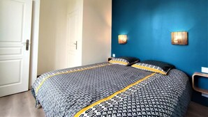 Une chambre à coucher avec un lit, une porte et un mur bleu orné de deux lampes fixées au mur.