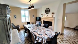 Une salle à manger avec un sol à carreaux, une longue table dressée pour quatre personnes et une cheminée.