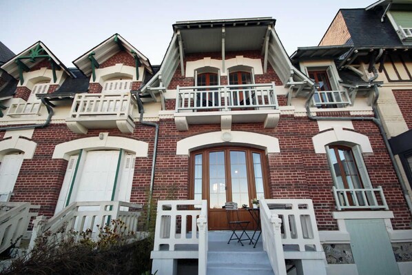 A two-story brick building with a central entrance, white railings, and a small balcony.