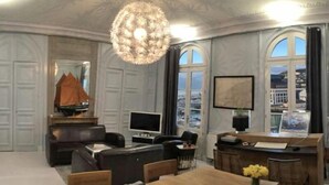A spacious room with a large chandelier, a dining area, a television, and a view of the city through large windows. - Norwegian Stern - Fecamp (FECAMP)