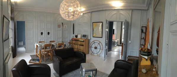 Een ruime woonkamer met een open haard, een eethoek met een tafel en stoelen, en een grote kroonluchter.