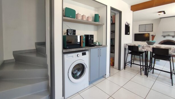 Een kleine keuken met een wasmachine, een magnetron en een koffiezetapparaat op het aanrecht.