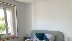 Een slaapkamer met een bed, houten vloeren, een raam en een nachtkastje.