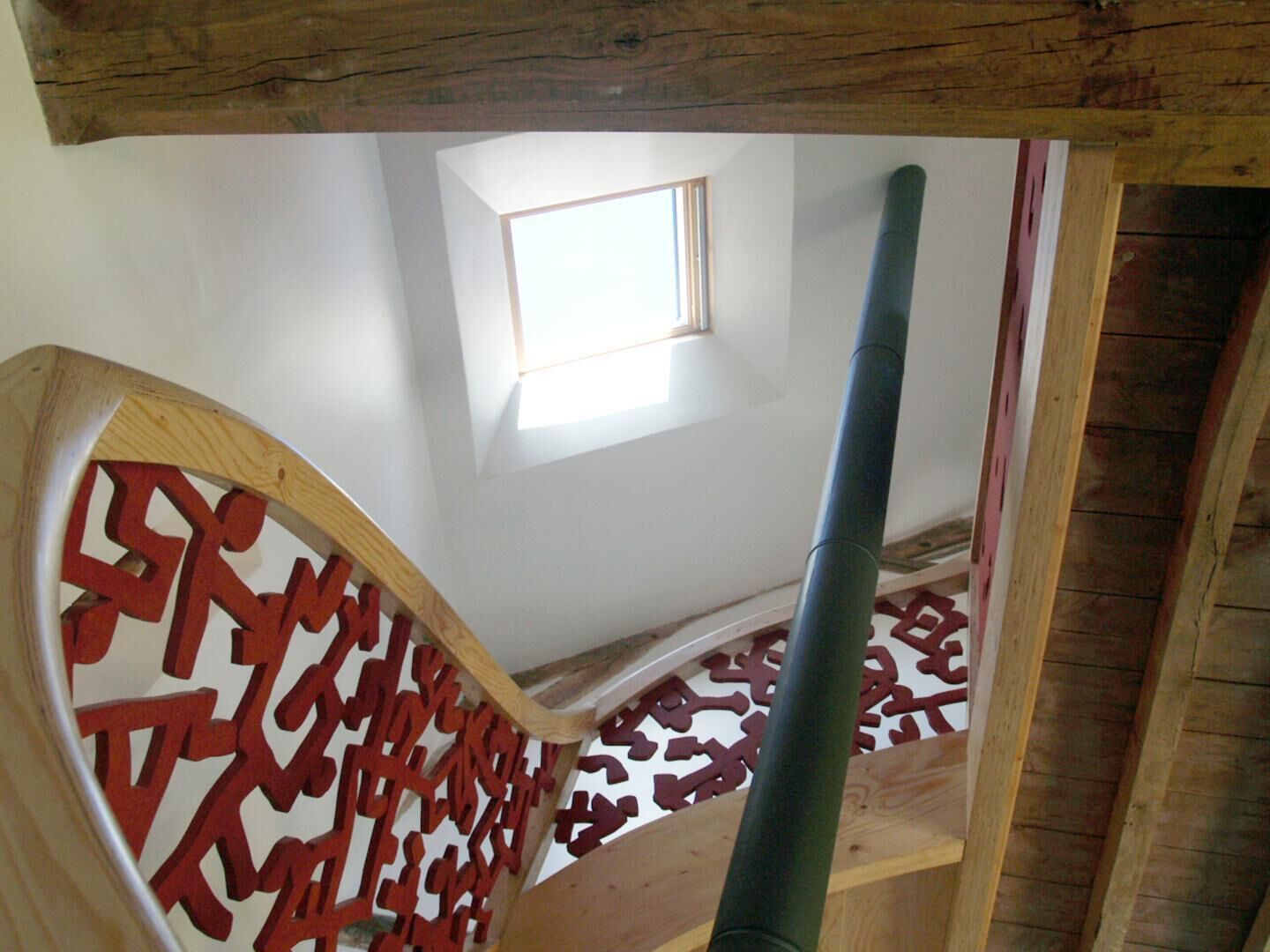 Una scala in legno con ringhiera a motivi geometrici e un piccolo lucernario.