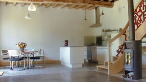 A modern interior with a dining area, kitchen, and a staircase with a wooden railing. - L'escarpolette - Riville (RIVILLE)
