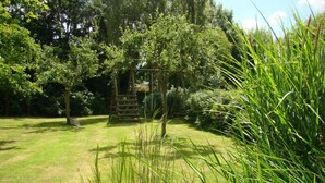 A garden with a wooden structure, lush greenery, and a clear sky. - L'escarpolette - Riville (RIVILLE)
