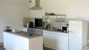 A modern kitchen with white cabinets, a central island, a stove, a microwave, and a refrigerator. - L'escarpolette - Riville (RIVILLE)