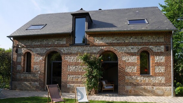 A brick building with two skylights, arched windows, and a small garden area with a chair and easel. - L'escarpolette - Riville (RIVILLE)