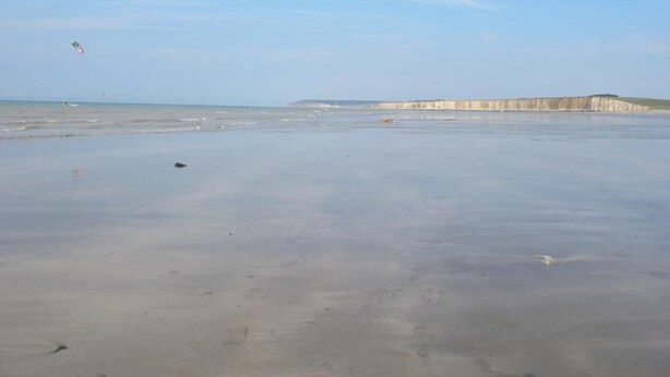 Een strand met een heldere lucht, kalme zee en verre kliffen.