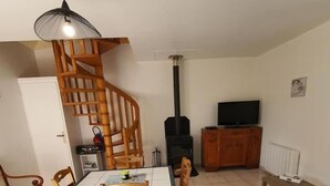 Een woonkamer met een eettafel, stoelen, een bank, een televisie, een open haard en een houten trap.