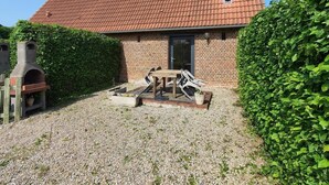 Een bakstenen huis met pannendak, een terras van baksteen en een houten tafel met stoelen.