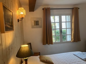 Een slaapkamer met een bed, een lamp, een raam met gordijnen, en een fotolijst aan de muur.