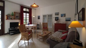 A living room with a sofa, two wicker chairs, a coffee table, a TV stand, a dining table with chairs, a red cabinet, and a lamp. - Chateau de La Croix Blanche (ST ARNOULT)