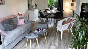 Un salon avec un canapé gris, un fauteuil blanc, une table à manger avec des chaises et une petite table basse.